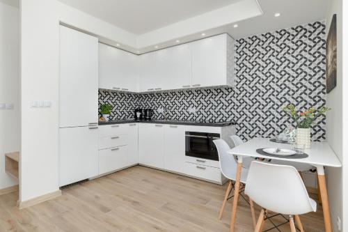 uma cozinha com armários brancos e uma mesa e cadeiras em Villa Tarsis Apartment in Kołobrzeg by Rent like home em Kolobrzeg