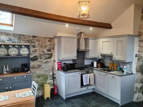 a kitchen with white cabinets and a stone wall at The Bothy in Caernarfon