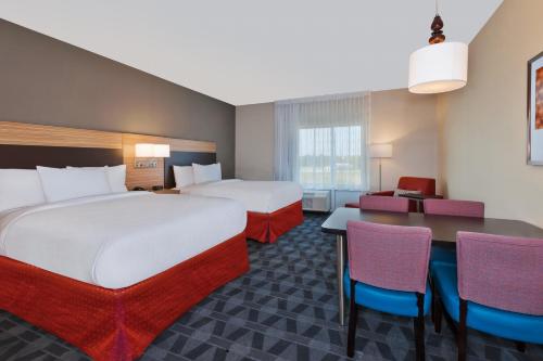 グランドラピッズにあるTownePlace Suites by Marriott Grand Rapids Airport Southeastのベッド2台、テーブルと椅子が備わるホテルルームです。