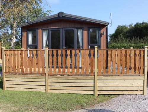 a wooden fence with a small cabin behind it at 26 Sherwood, South Lakeland Leisure Village in Carnforth