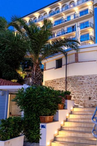 a hotel facade with stairs and a palm tree at Grand Hotel Santa Maria in Santa Maria di Castellabate