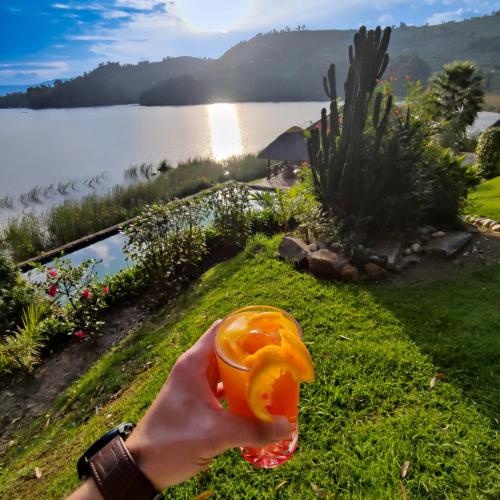 a person holding a drink in a cup in front of a lake at Birdnest Resort in Kabale