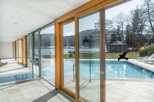 a house with glass walls and a swimming pool at Seehotel Urban in Bodensdorf