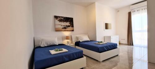 two beds in a white room with blue sheets at Seaside Serenity - Luxe Penthouse - near the beach by QuickTrips in Mellieħa