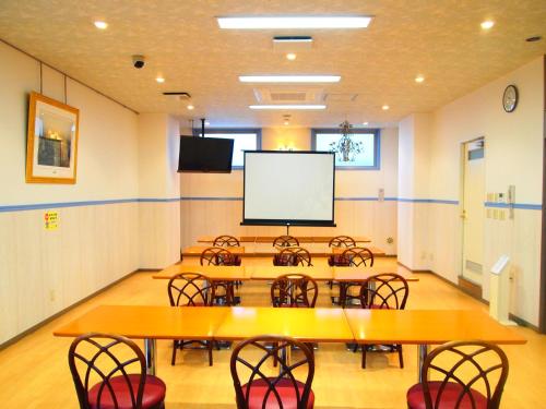 a conference room with tables and chairs and a screen at Hotel Sunrise21 in Higashihiroshima