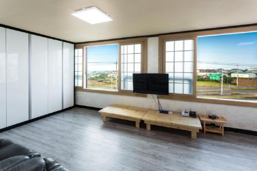 a living room with a couch and a tv and windows at Jeju Wayo Pension in Jeju