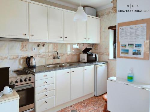 a kitchen with white cabinets and a sink and a microwave at Mira'Barrinha Flats in Praia de Mira