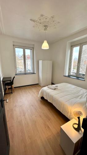 a bedroom with a bed and a table and windows at Appartement F5 proche centre ville in Mulhouse