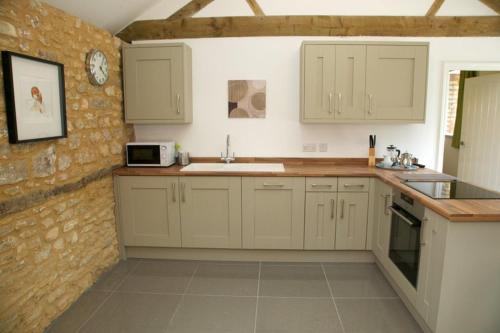 uma cozinha com armários brancos e uma parede de tijolos em Mouse House at Tove Valley Cottages em Towcester