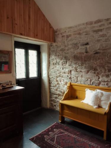 Cette chambre dispose d'un canapé jaune et d'un mur en pierre. dans l'établissement Loft les Noies Parrons, gîte aux milles étangs, à Mélisey