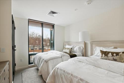 a white bedroom with two beds and a window at Treehouse at Spruce Peak in Stowe