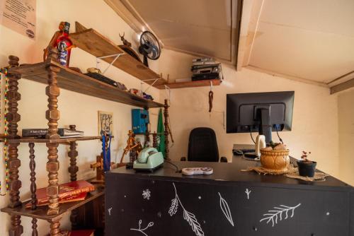 a room with a desk with a computer and a tv at Hostel Raízes in Brumadinho