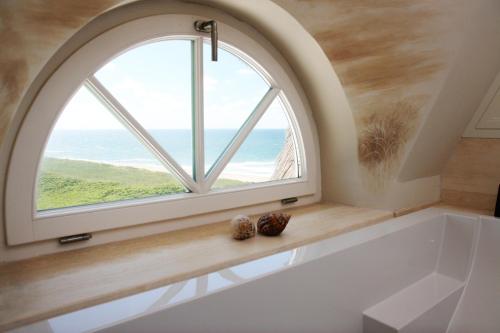 an arched window in a bathroom with a bath tub and a large window at Söl'ring Hof in Rantum