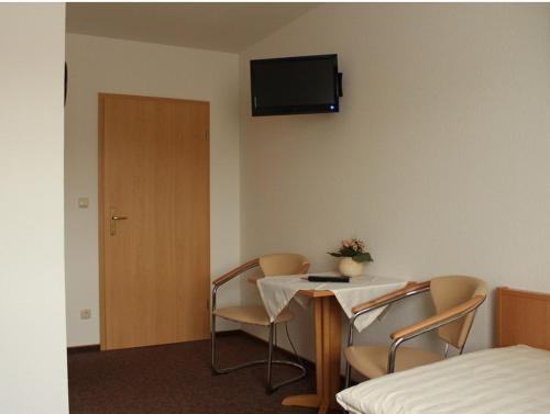 Cette chambre dispose d'une table, de chaises et d'une télévision murale. dans l'établissement Gästehaus Zum Felsenkeller, à Nordhausen