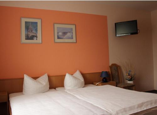 - une chambre avec un lit blanc et un mur orange dans l'établissement Gästehaus Zum Felsenkeller, à Nordhausen