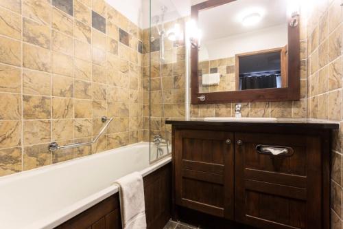 ein Badezimmer mit einer Badewanne, einem Waschbecken und einem Spiegel in der Unterkunft Résidence Les Arcs Le Village - maeva Home - Pièces Prestige 61 in Bourg-Saint-Maurice