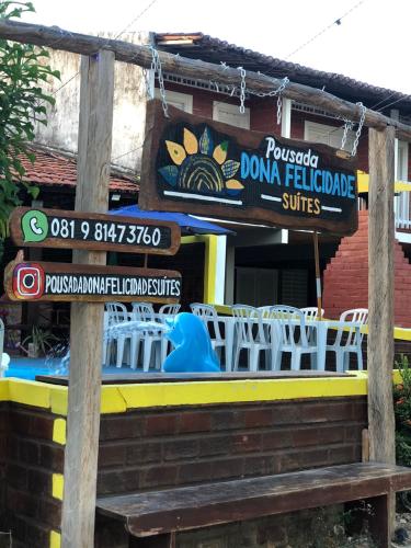 a sign in front of a restaurant with a table and chairs at Pousada Dona Felicidade Carneiros in Tamandaré