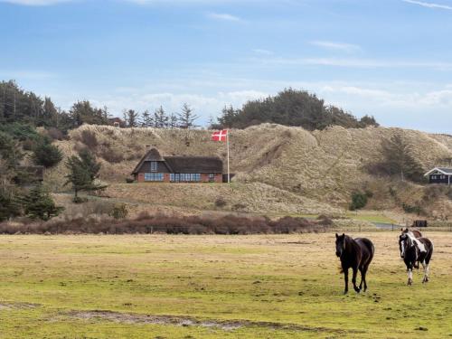 dois cavalos num campo com uma casa ao fundo em Holiday Home Damiana - 600m from the sea in NW Jutland by Interhome em Blokhus