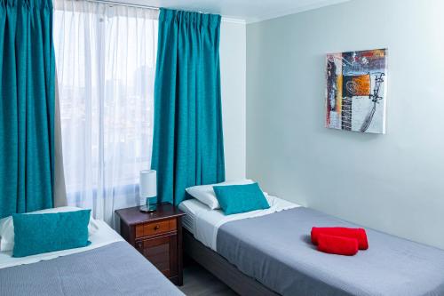 um quarto com 2 camas e uma janela com cortinas verdes em Departamentos Amoblados Torre Tagle em Santiago