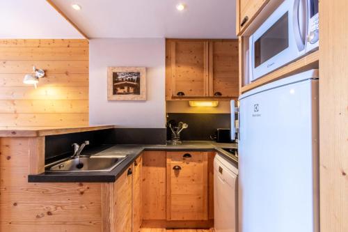 une cuisine avec des armoires en bois, un évier et un réfrigérateur dans l'établissement Résidence Les Néreïdes - maeva Home - Appartement 3 pièces 7 personnes - Prestige MAE-2704, à La Plagne Tarentaise
