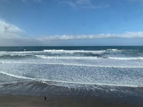 a person standing on the beach with a surfboard in the ocean at West Beach Suites in Lincoln City