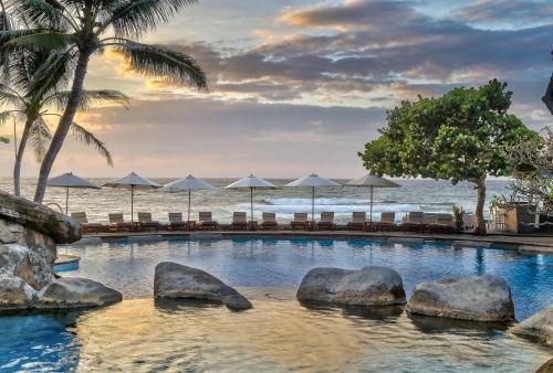 a swimming pool next to the ocean with chairs and umbrellas at Hilton Bali Resort in Nusa Dua