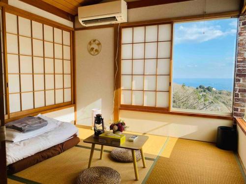 een kamer met een bed, een tafel en ramen bij 熱海星海台 星の輝きを導く石の小道 海景BBQの空間 大島を望む 日の出と夜景 in Atami