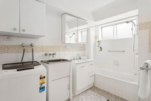 a white bathroom with a sink and a bath tub at Mid-Century Morningside 2-Bed Apartment in Brisbane