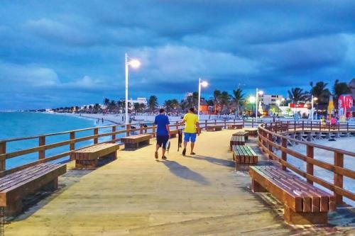 zwei Menschen, die auf einem Pier neben dem Meer laufen in der Unterkunft Cómodo Departamento a 2 cuadras de la playa in Progreso