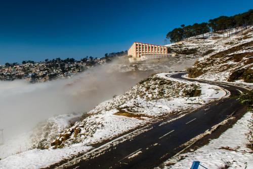 a road with snow on the side of a mountain at Binsar Eco Resort, Binsar - Uttarakhand in Hawālbāgh
