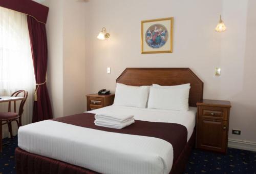 una habitación de hotel con una cama grande con sábanas blancas en Palais Royale, en Katoomba