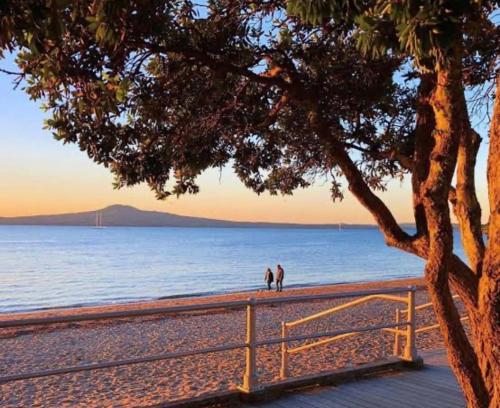 two people standing on a beach near the water at Delightful little house & Chateau Charme Suite in Auckland