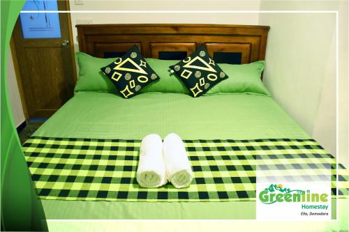 a green bed with green pillows and two slippers on it at Greenline Homestay in Demodera