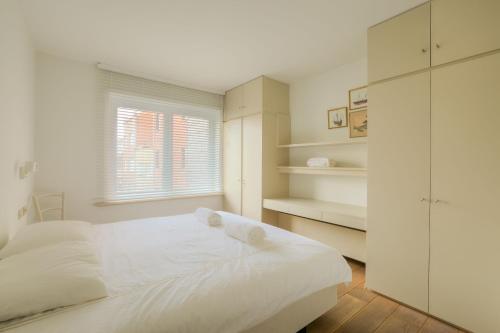 een witte slaapkamer met een bed en een raam bij 4e verdiep appartement met zeezicht in Knokke in Knokke-Heist