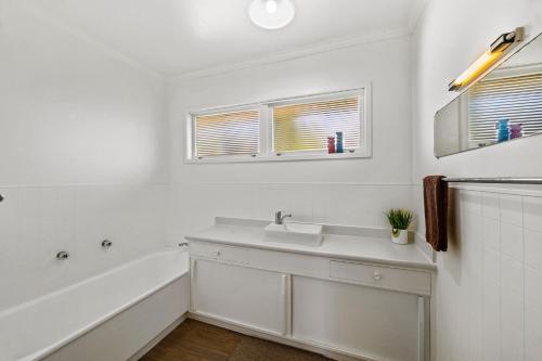 a white bathroom with a sink and a tub at Red Brick Cottage-First choice for families in Rotorua