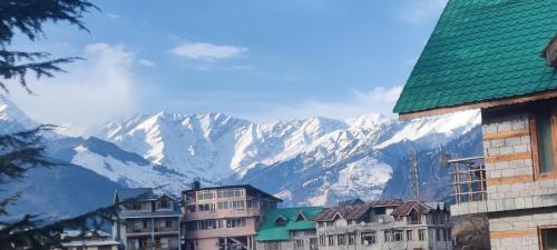 un groupe de bâtiments avec des montagnes en arrière-plan dans l'établissement Madana Inn Manali, à Manali