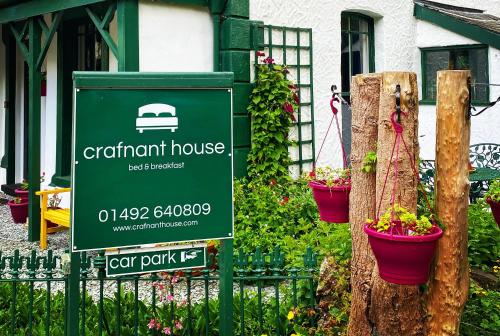 a green sign in front of a house with potted plants at Crafnant House - Bed & Breakfast in Trefriw