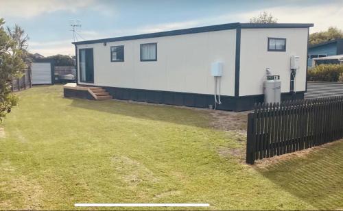 a small white house with a fence in a yard at Cute little Foxton Beach bach in Foxton Beach