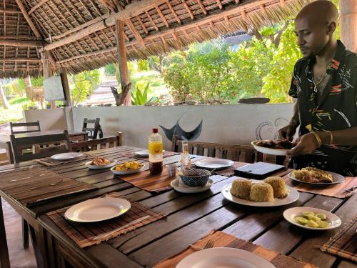 a man standing at a wooden table with plates of food at Sazani Beach Lodge and Tidal Lounge in Nungwi