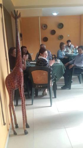 Heritage Hotel Rukungiri في Rukungiri: مجموعة من الناس يجلسون على طاولة مع زرافة وهمية