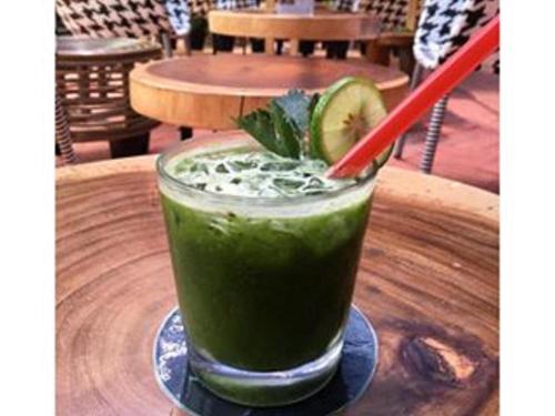 uma bebida verde com uma palha vermelha numa mesa de madeira em Couleur Hotel Cengkareng em Jakarta