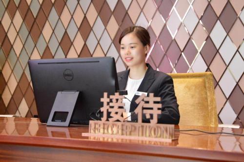 a woman sitting at a desk with a laptop computer at Yongzhou Chuang Fa Cheng XiaoXiangYi Hotel in Guzhuting