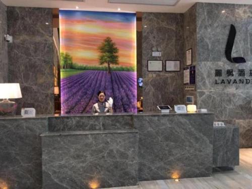 a man standing in a lobby with a large painting on the wall at Lavande Hotel Yichang Railway East Station Branch in Baiyang