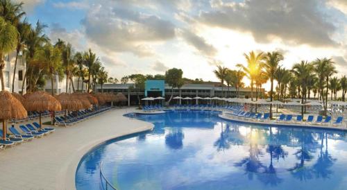 a large pool with chairs and umbrellas and palm trees at Riu Yucatan - All Inclusive in Playa del Carmen