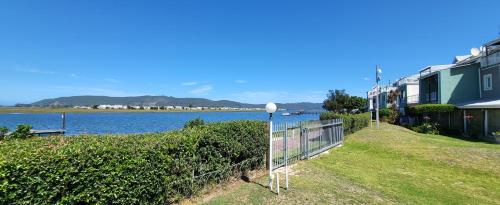 uma casa com uma cerca ao lado de uma massa de água em Casa de Pueblo Knysna Views! em Knysna