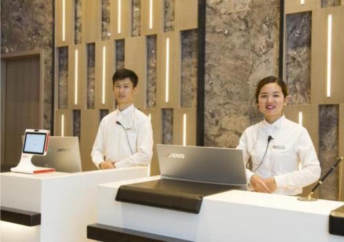 two people standing at a counter with a laptop at Echarm Hotel Beihai Yintan in Dianbailiao