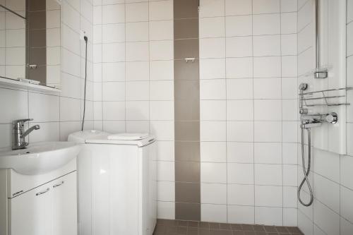 uma casa de banho em azulejos brancos com um lavatório e um chuveiro em Kotimaailma Apartments Kamppi - 2BR in the city center with code lock em Helsinque