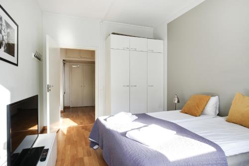 a white bedroom with a bed and a television at Kotimaailma Apartments Kamppi - 2BR in the city center with code lock in Helsinki