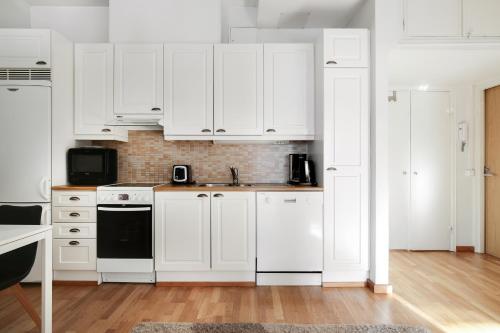 a white kitchen with white cabinets and a sink at Kotimaailma Apartments Kamppi - 2BR in the city center with code lock in Helsinki