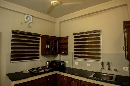 a kitchen with wooden cabinets and a sink and two windows at Siby Homestay in Ernakulam